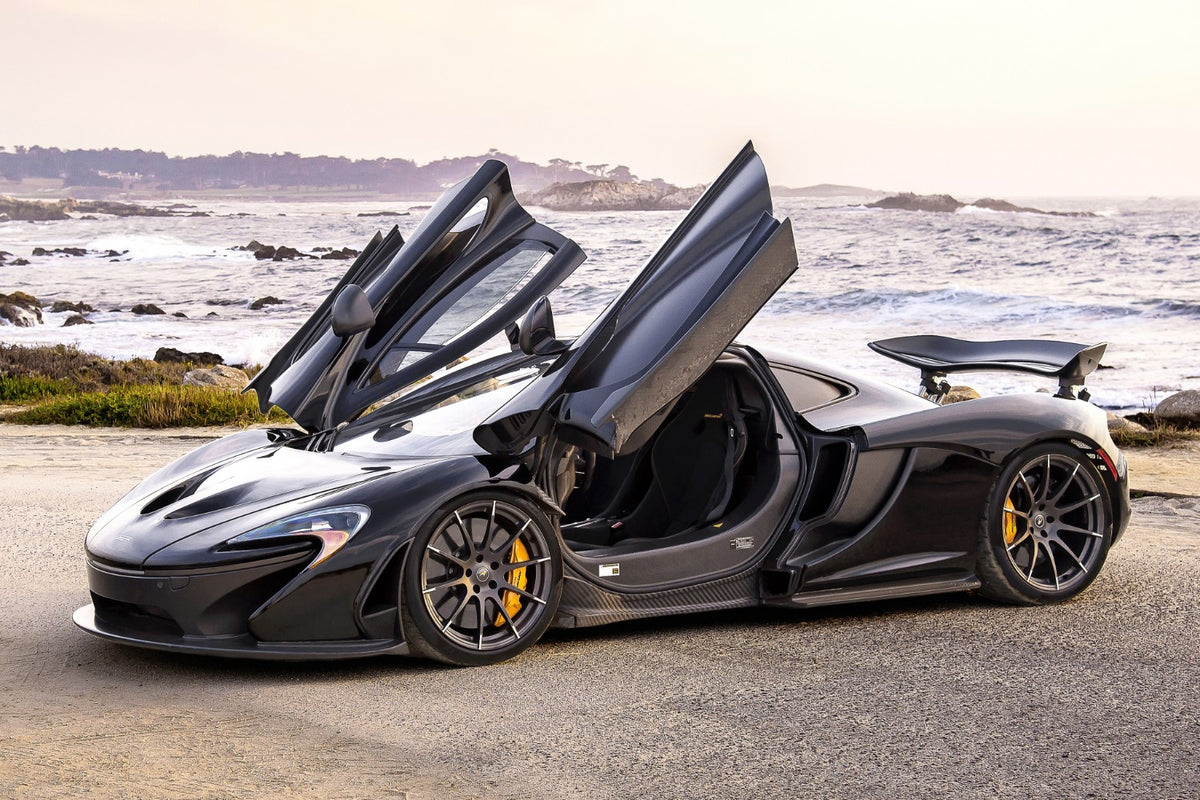 Black McLaren P1 with dihedral doors open on the coast at Pebble Beach